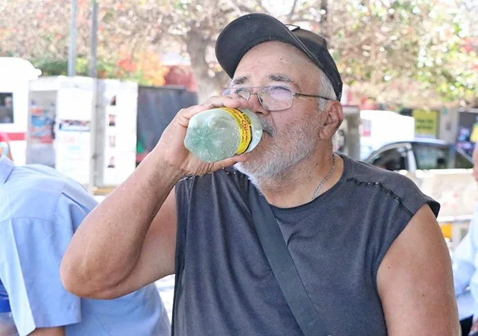 Personas se cubren del sol y beben agua durante un día de altas temperaturas en Baja California Sur.